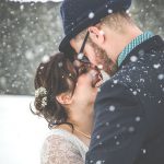 Hochzeitspaar im Schneefall unter Schirm